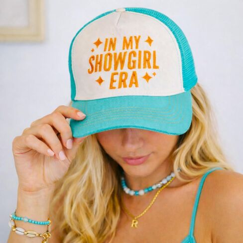 قبعة سائق الشاحنة باللون الأزرق المخضر والأبيض مع نص برتقالي لامع في نص My Showgirl Era، وخياطة متباينة، وقبعة بيسبول بموضوع الحفل الموسيقي in Saudi Arabia